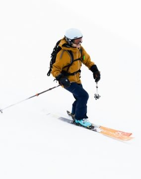 Female skier in a bright yellow jacket skiing down a snowy slope